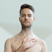 Geoff Lester standing with bare chest, hand on heart, heart surgery scar 