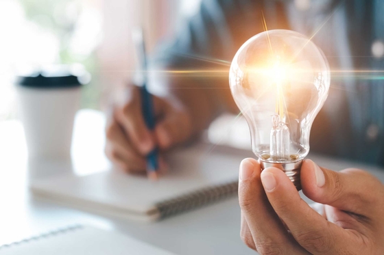 Person writing with one hand, the other is holding a brightened light bulb in their hand