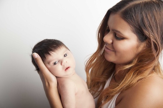 A young First Nations mother holds her new born baby and looks at them lovingly